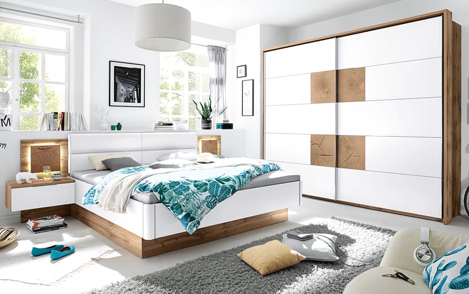 schlafzimmer in weiss und eiche mit beleuchtetem bettkopfteil und schwebetuerenschrank