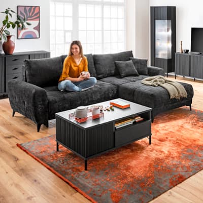 frau sitzt entspannt auf dunkelgrauem sofa in modernem wohnzimmer